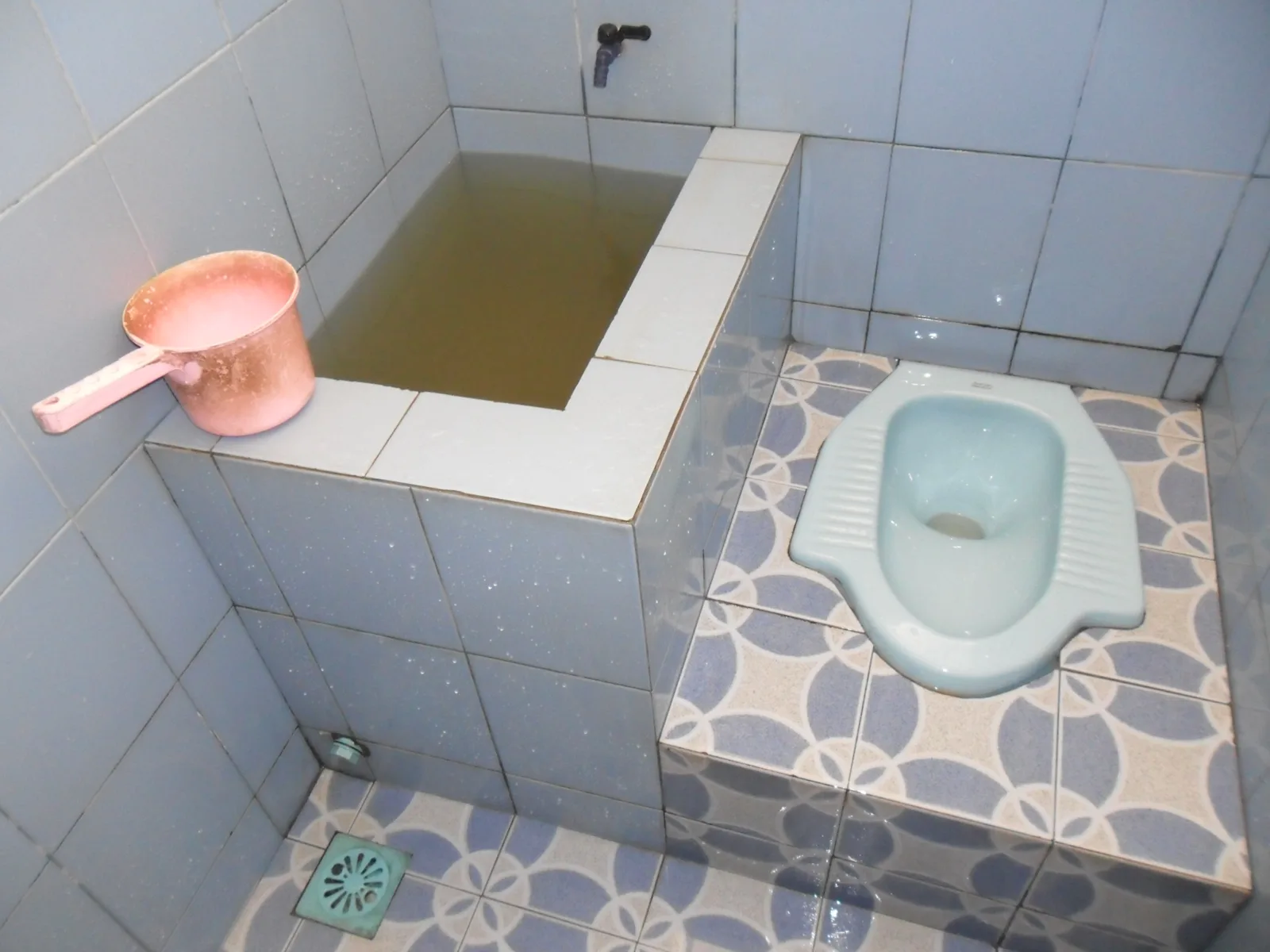 Kamar mandi dengan kloset jongkok, bak air, kran dinding, dan lantai keramik sebagai ilustrasi; bukan lokasi proyek Inproland
