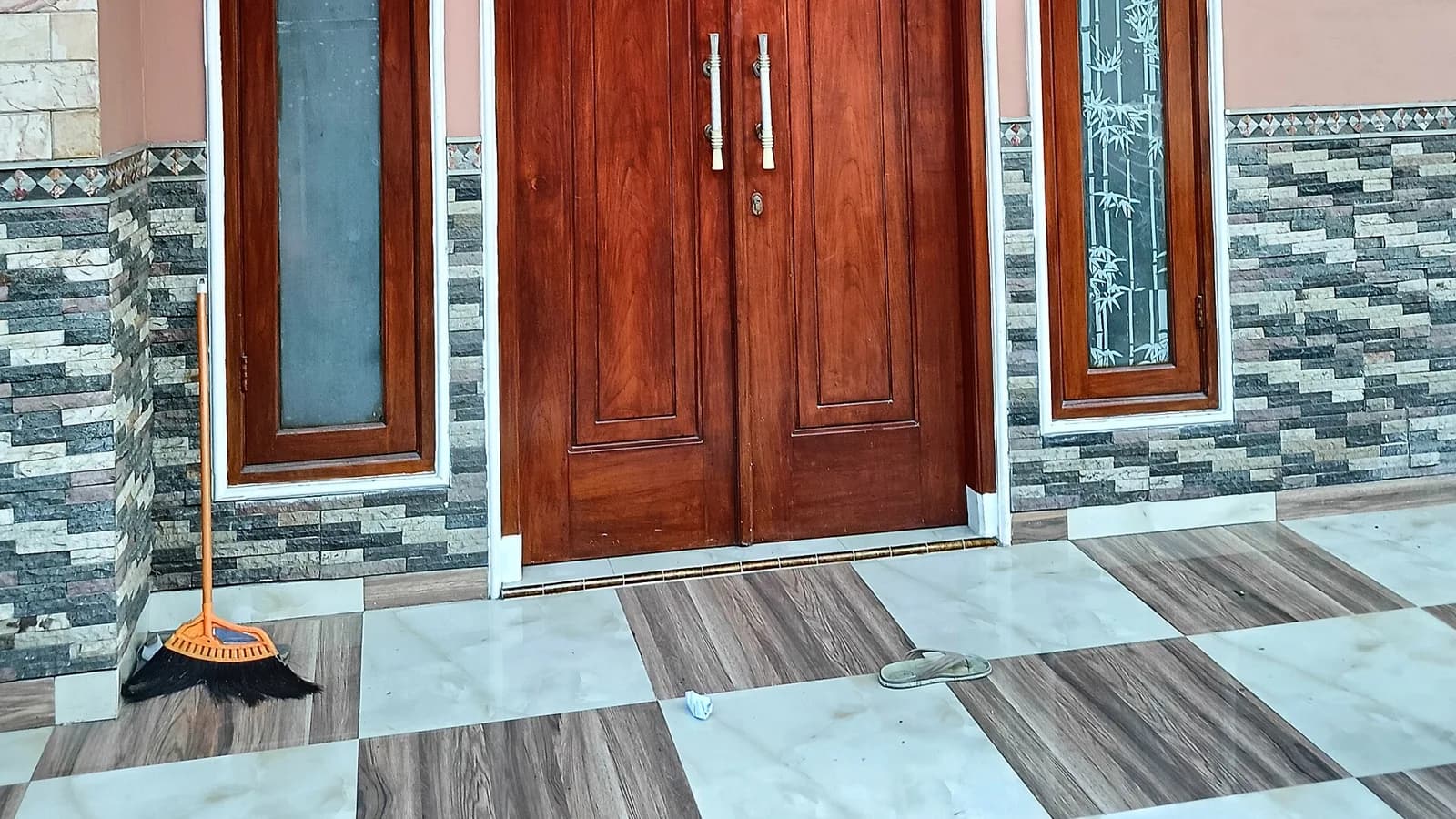 Pintu utama kayu ganda dengan dua jendela samping di teras rumah perumahan beralas keramik