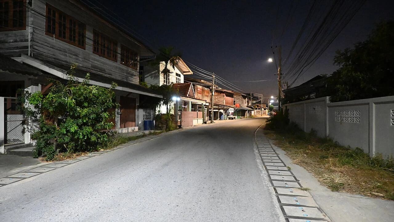 Jalan perumahan malam hari dengan saluran tertutup dan lampu jalan